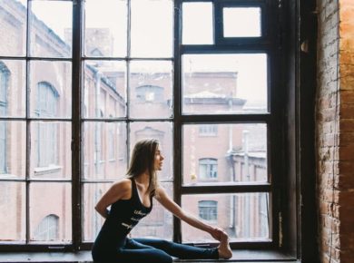 stretching woman in workout gear in front of window old building cityscape behind